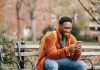 delightful african american man surfing modern cellphone in city park